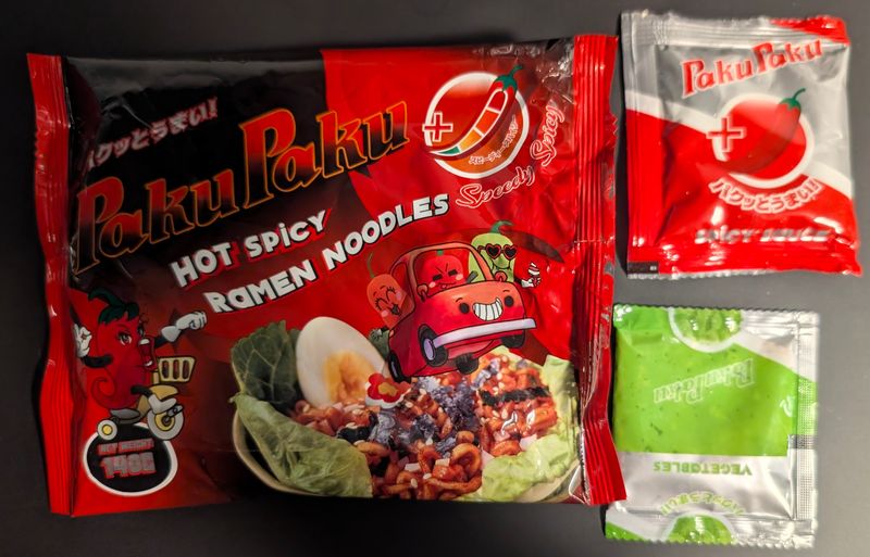 Paku Paku - Speedy Spicy Hot Spicy Ramen Noodles Packung, daneben die Packung sowie Soßen- und Gewürzbeutel