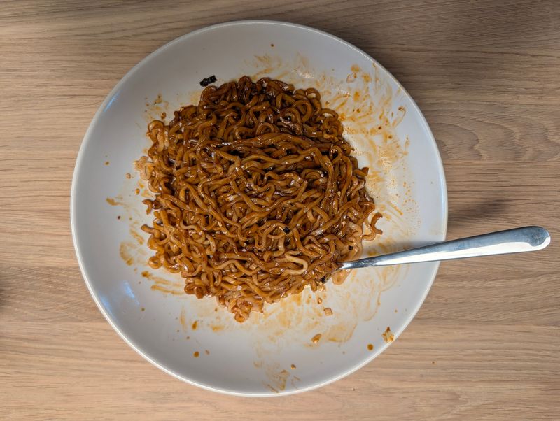 Paku Paku - Speedy Spicy Hot Spicy Ramen Noodles: Fertig gekochte, gut vermischte Nudeln mit brauner Soße auf dem Teller von oben