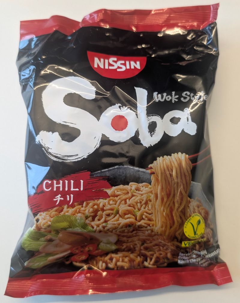 Nissin Soba Chili Wok-Style: schwarze Packung mit rotem Chili-Schriftzug und Nudeln auf dem Etikett