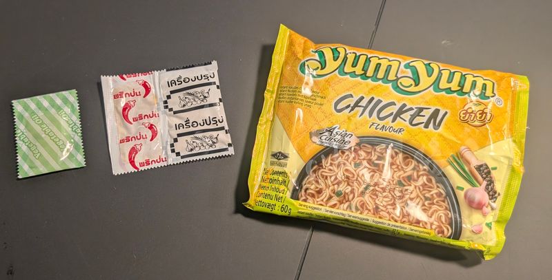 Päckchen mit Pflanzenöl und Doppelbeutel mit Chili- und Gewürzmischung neben der Yum Yum Chicken Packung