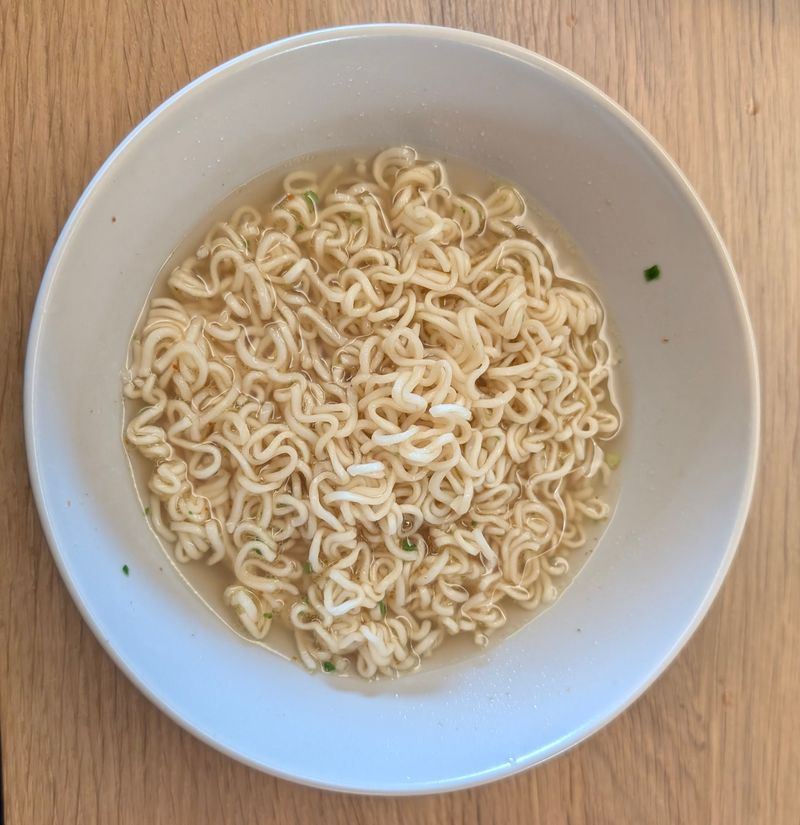 Fertige Yum Yum Chicken Nudeln in heller Brühe in einer weißen Schale auf einem Holztisch